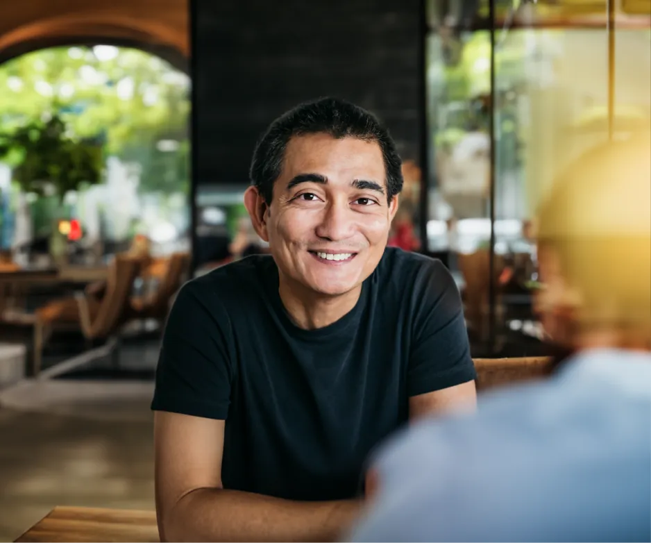 The man wearing glasses smiling as he converses, with a blurry, ethereal figure floating in front of them