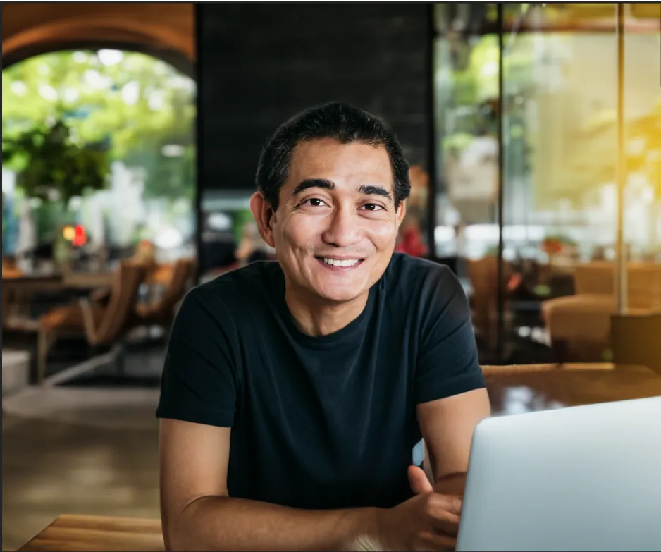 The man wearing glasses smiling as he converses, with a natural looking background and foreground. However, the man's fingers look incorrect and unnatural.