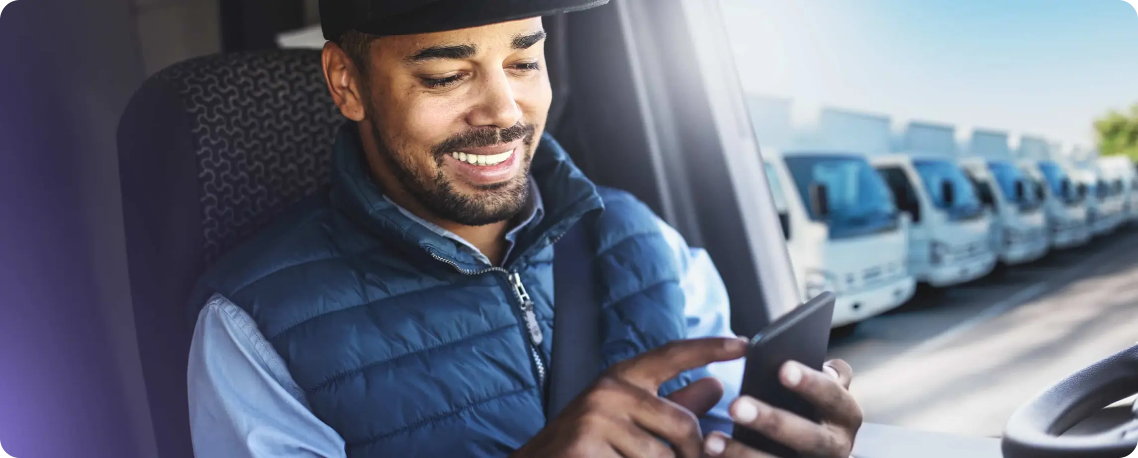 Trucker in cabin of truck, parked at a parking lot and checking their phone with a smile