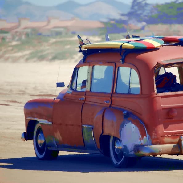 An old (but reliable) car cruising down the beach, with surfboards strapped to its roof.