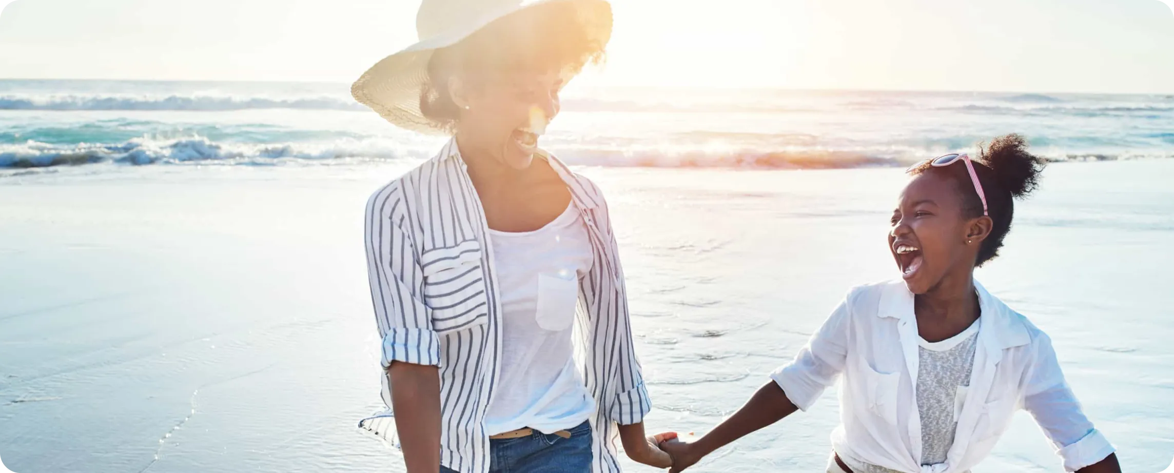 Mother and daughter holding hands and laughing on the beach during sunset