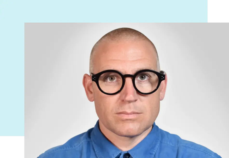 Nick Foster wearing a blue button up shirt and styish, round glasses