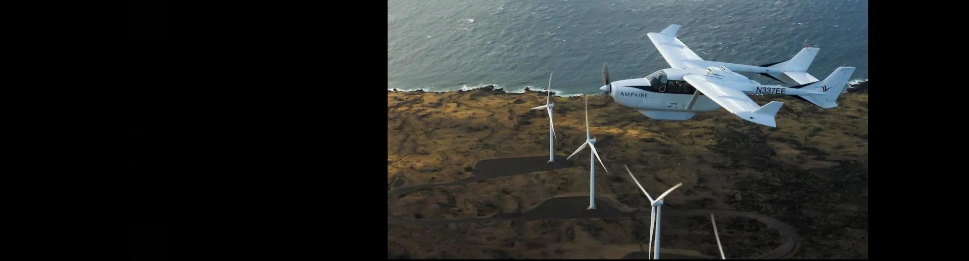 An airplane flies over a field of wind turbines. The photo is placed in a panoramic banner, with large black bars on either side